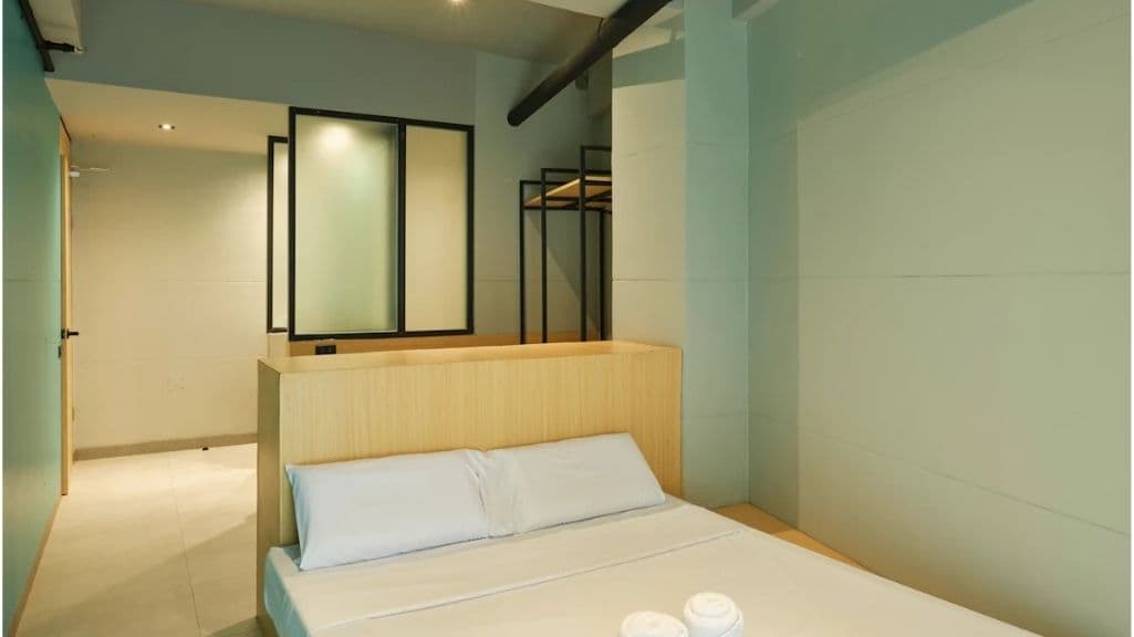 A double room with white linen against a pale timber slatted headboard wall, rolled towels at the foot of the bed and mint-green walls.