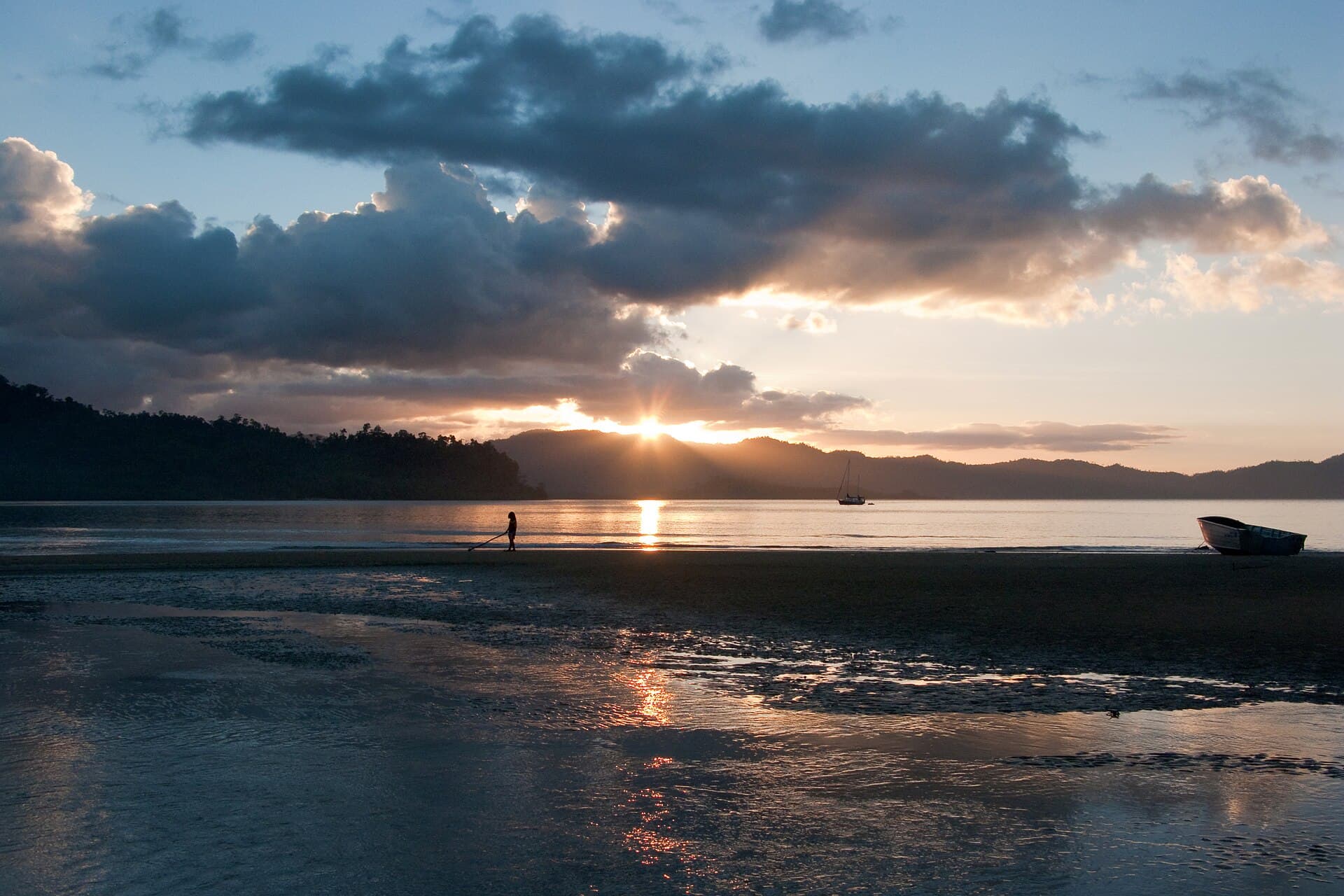 Sunset over Port Barton bay at low tide, a lone figure walking the exposed sand bar and a yacht moored offshore.